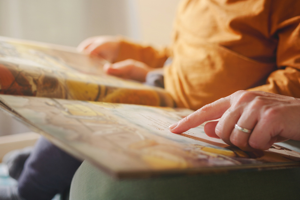 A mother's finger points to a page in a book as she explains a story to her son who is sitting on her lap